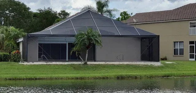 A house with a screened in porch is sitting next to a body of water.