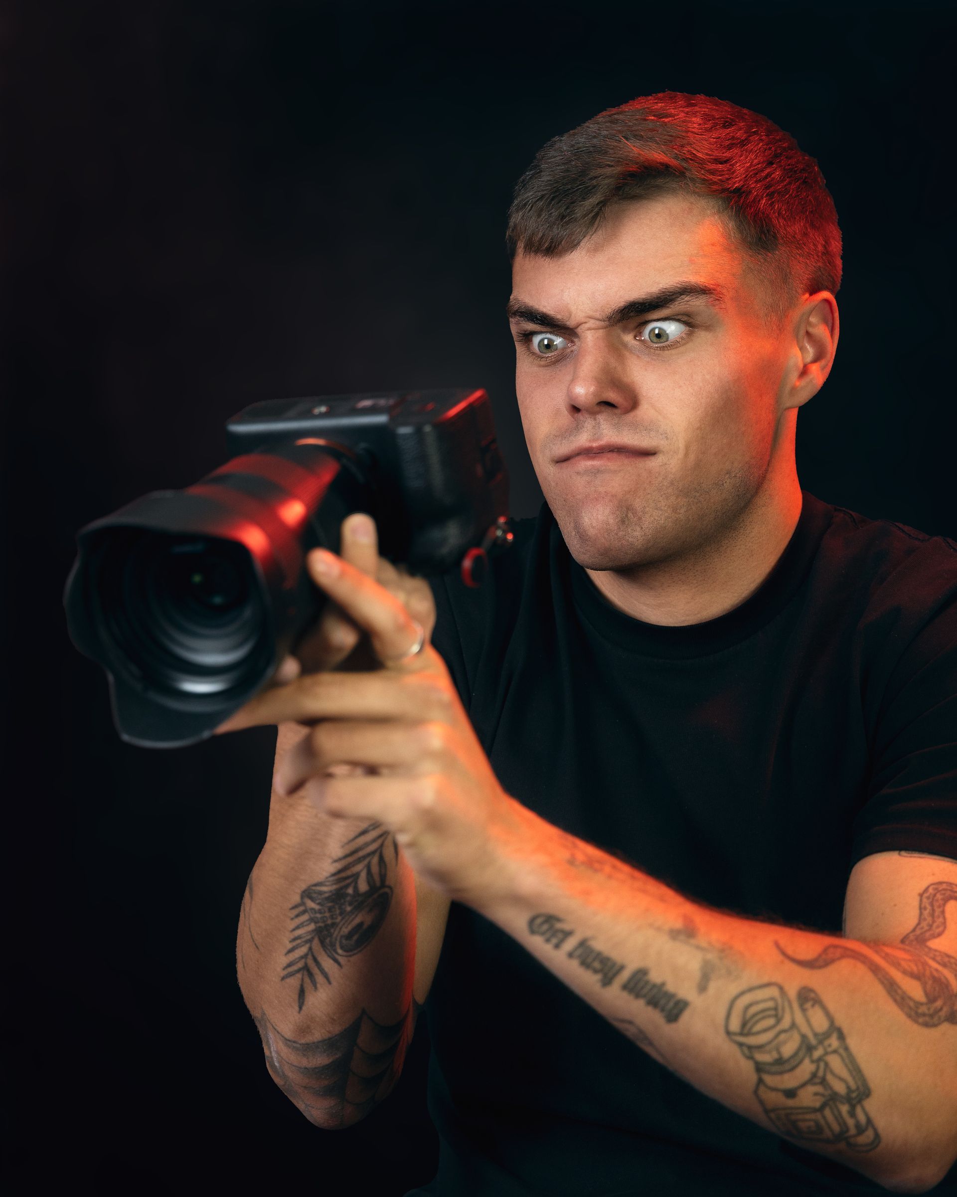 A man with tattoos is holding a camera and making a funny face.