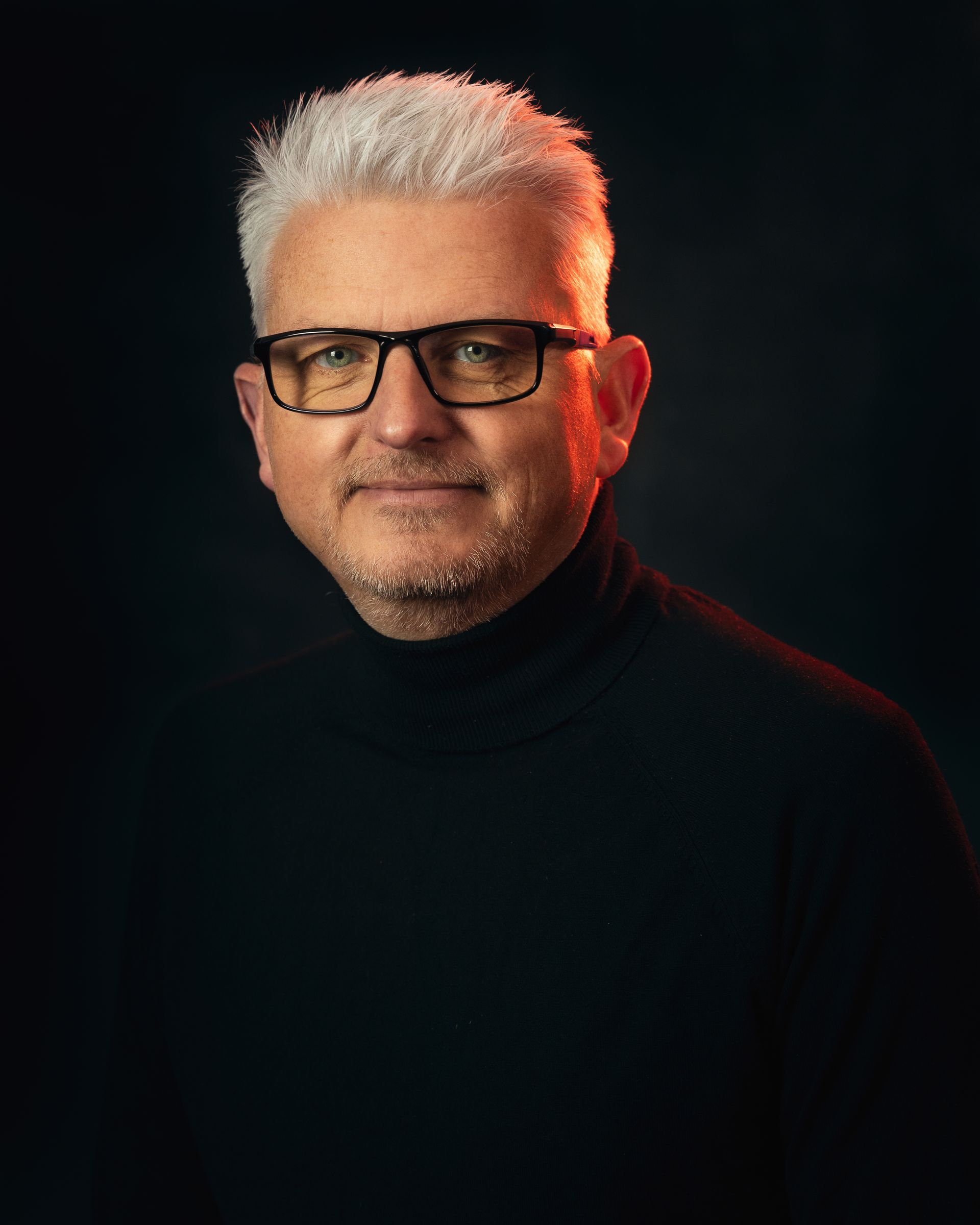 a man wearing glasses and a black turtleneck is looking at the camera .