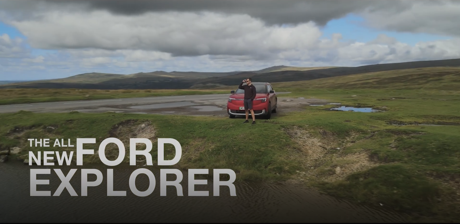 A man is standing next to a red ford explorer in a field.