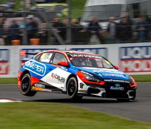 Blue and orange race car speeding on a track with blurred spectators in the background