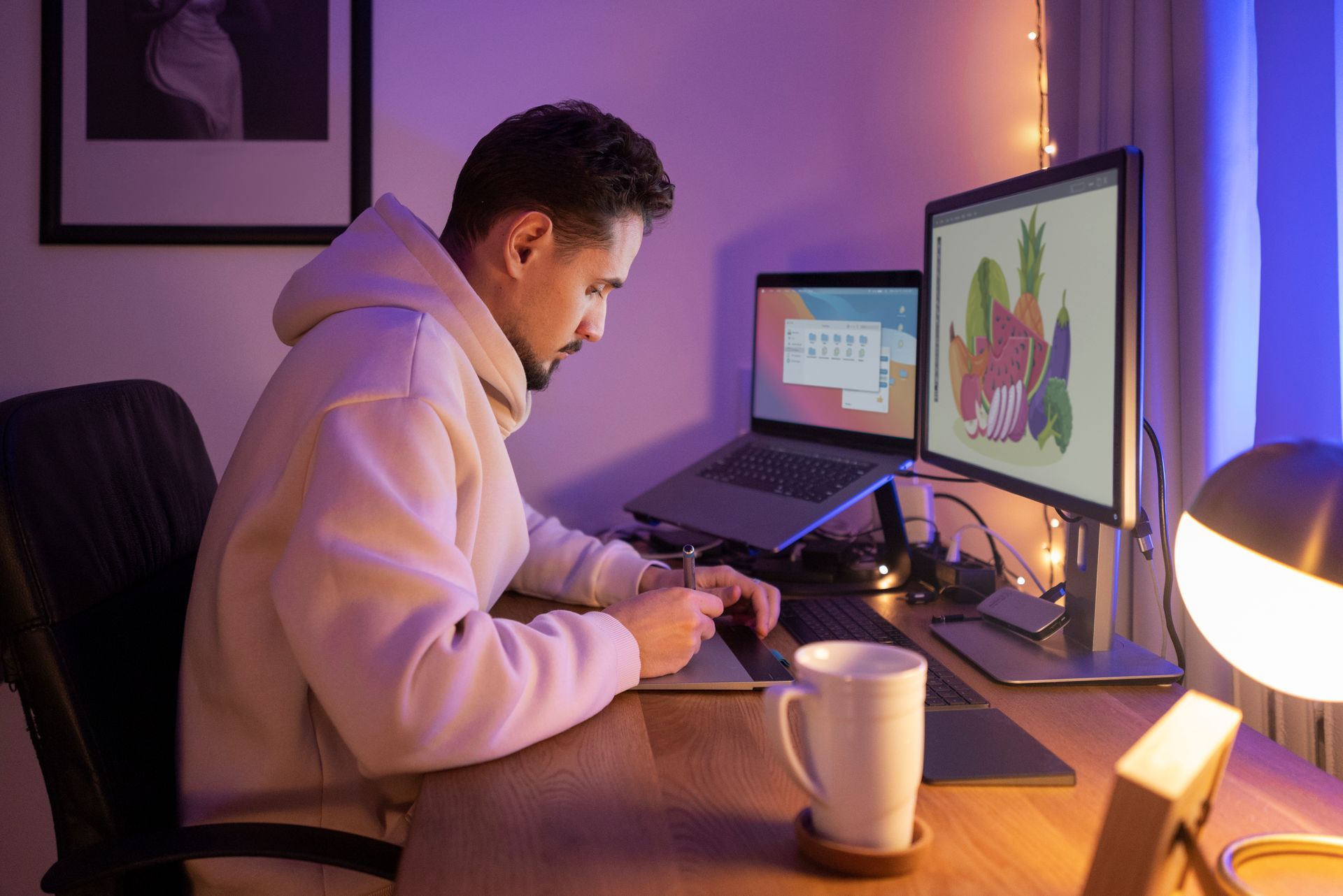 A man is sitting at a desk with a laptop and two computer monitors.
