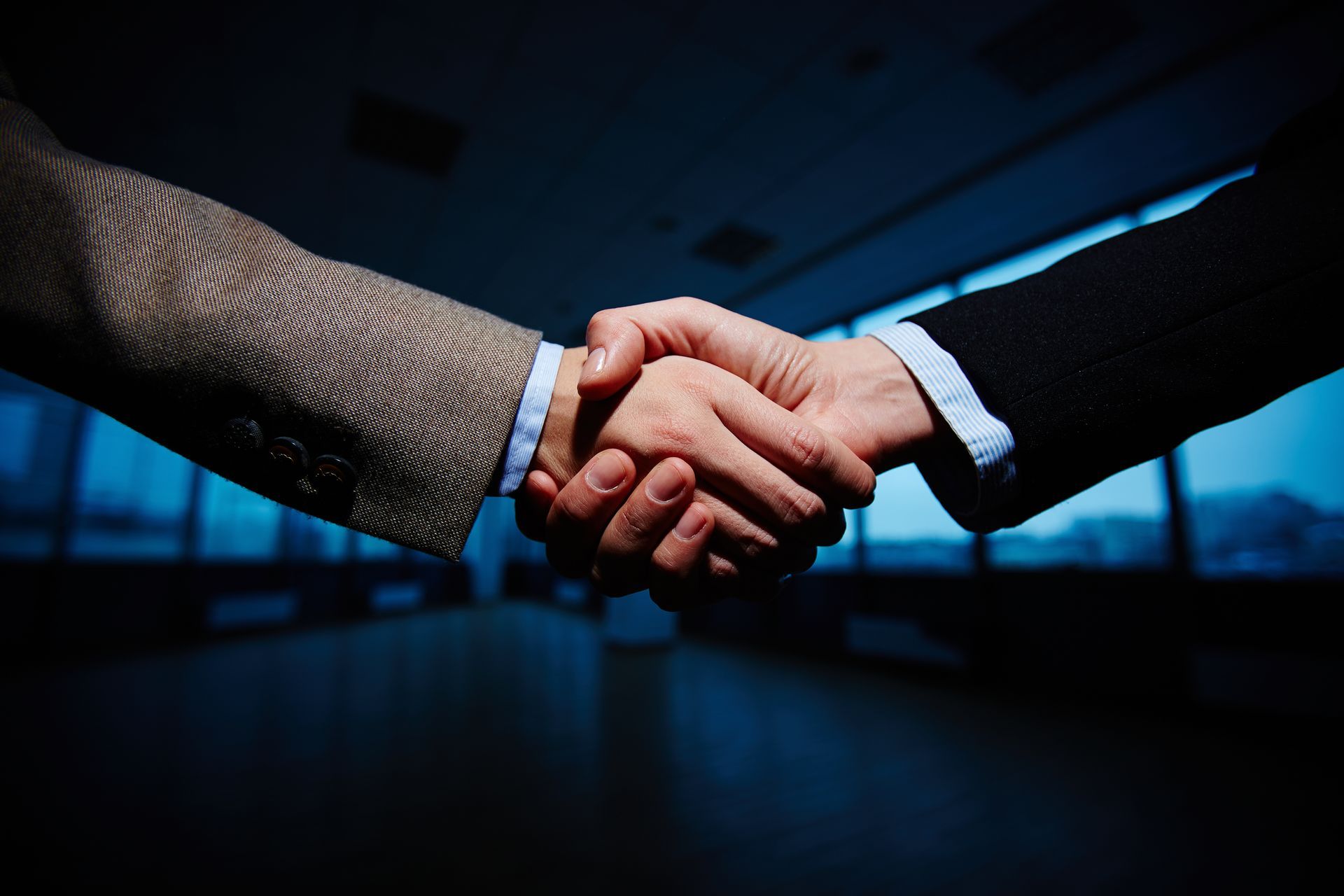 Two people in suits shaking hands in an office setting, signifying a deal or agreement.