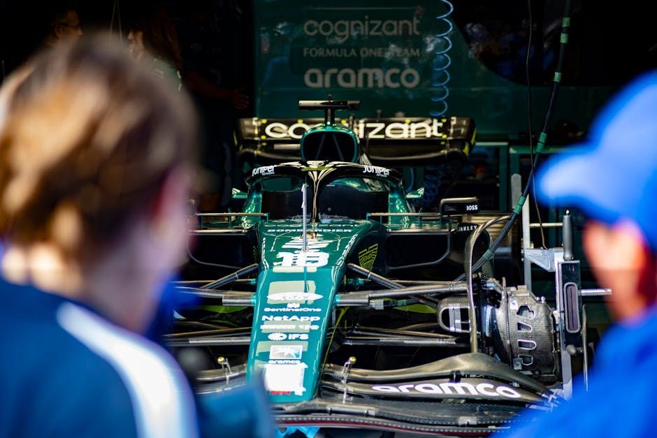Aston Martin Formula 1 car in green garage, crew members in foreground.