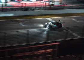 Race car speeding on a wet track at night, motion blur and bright headlights glowing