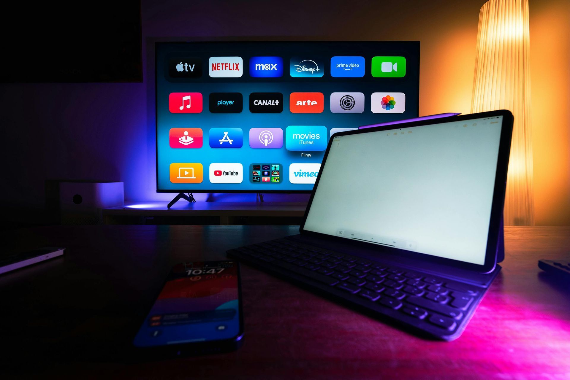 A laptop is sitting on a desk next to a phone and a television with logos of tv streaming services.