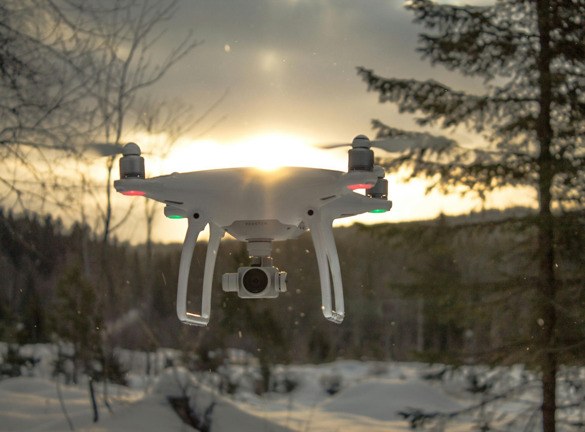 A drone is flying over a snowy forest at sunset.