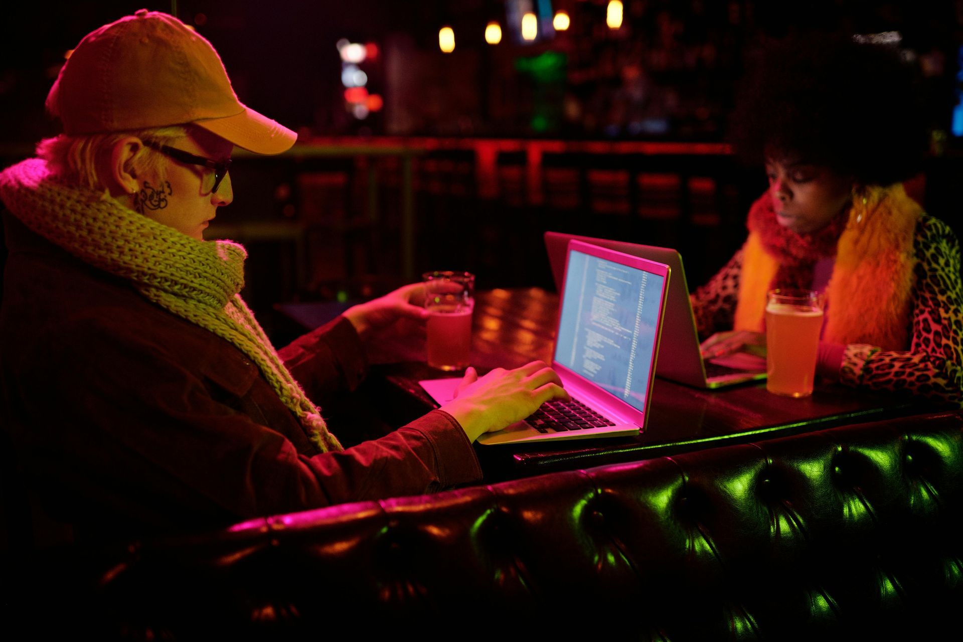 A man is sitting at a table with a laptop and a glass of beer.