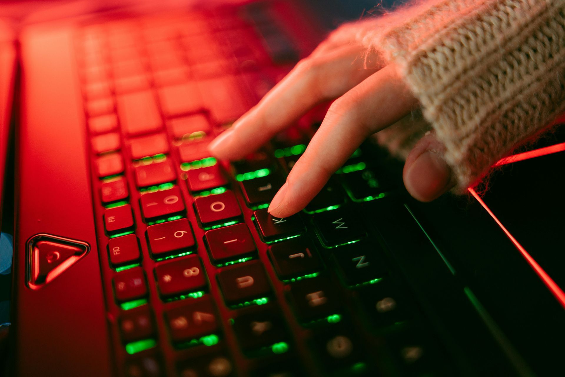 A person is typing on a laptop computer with green lights on the keyboard.