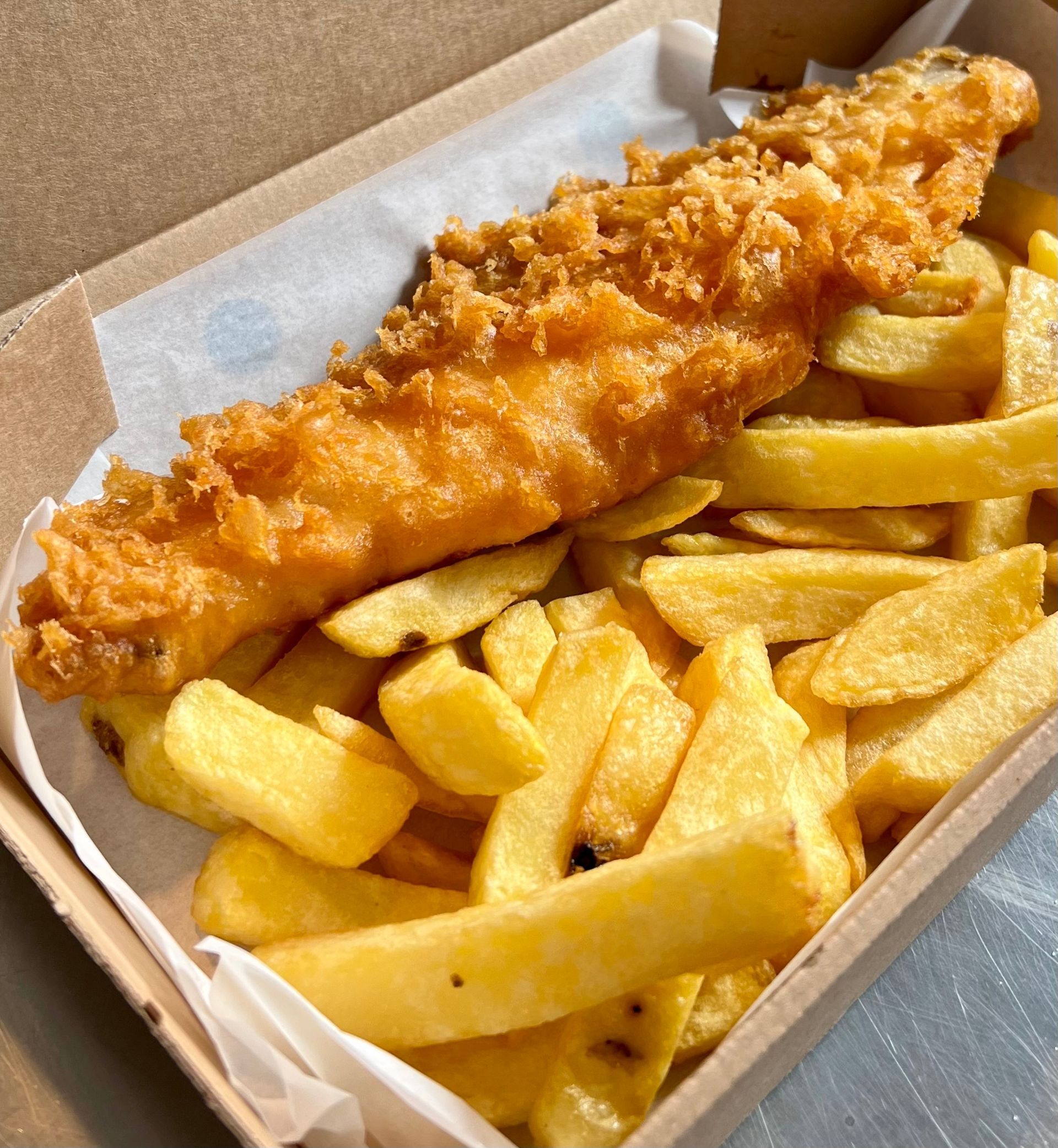 A box of fish and chips with a piece of fish on top