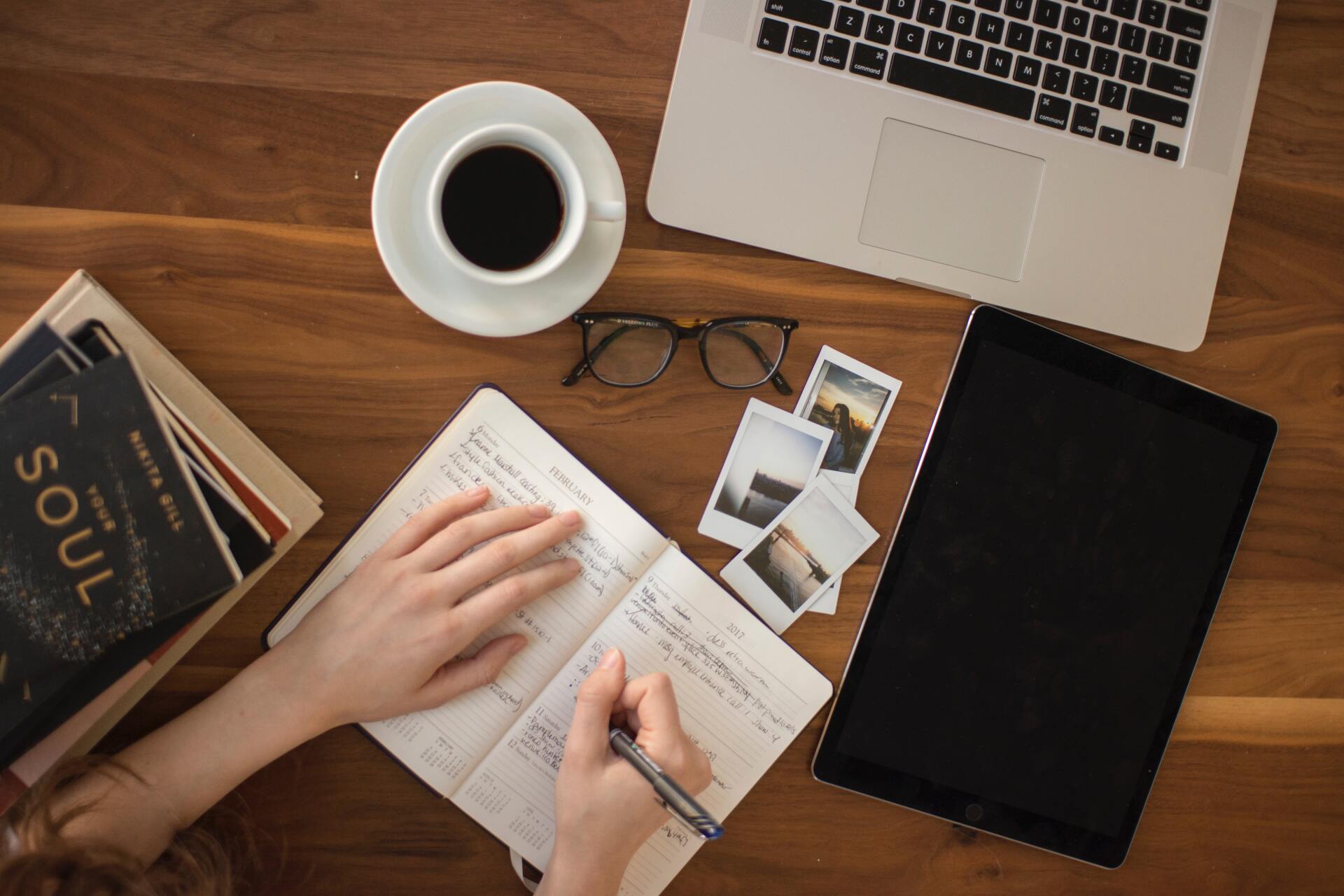 a person is writing in a notebook next to a laptop and a tablet .