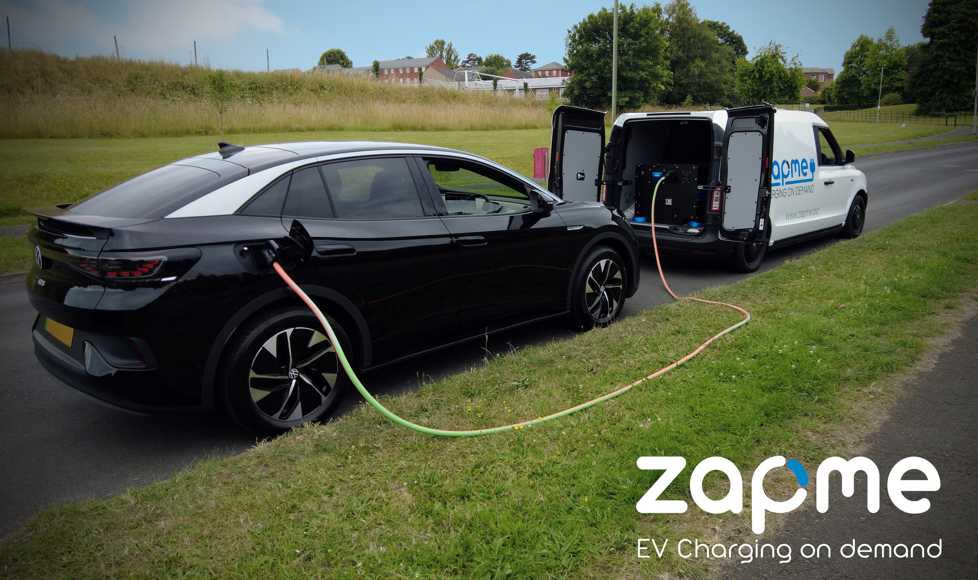 A black electric car is being charged  by a white van holding a rapid EV charger.