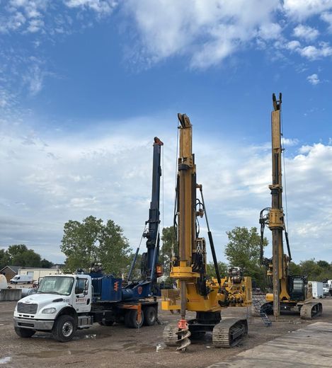 Three construction vehicles are parked in a dirt lot
