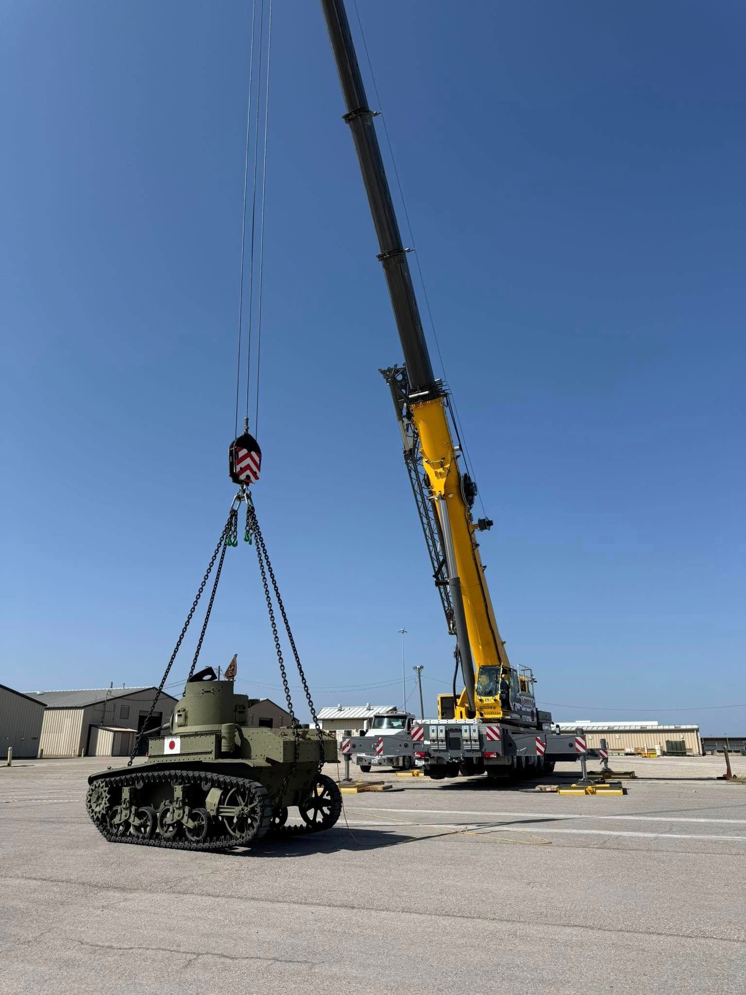 A tank is being lifted by a crane in a parking lot.