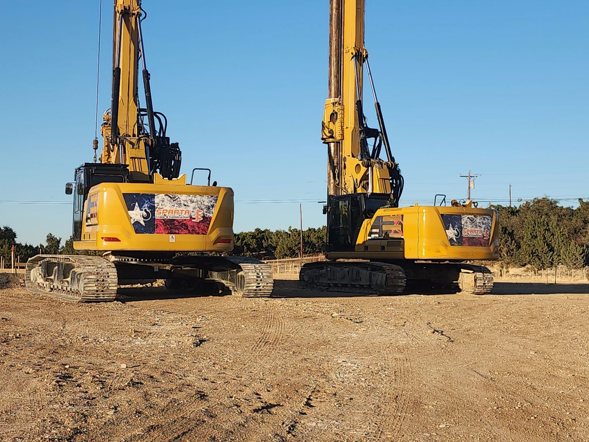 Two yellow excavators with texas flags on them are parked in a dirt field