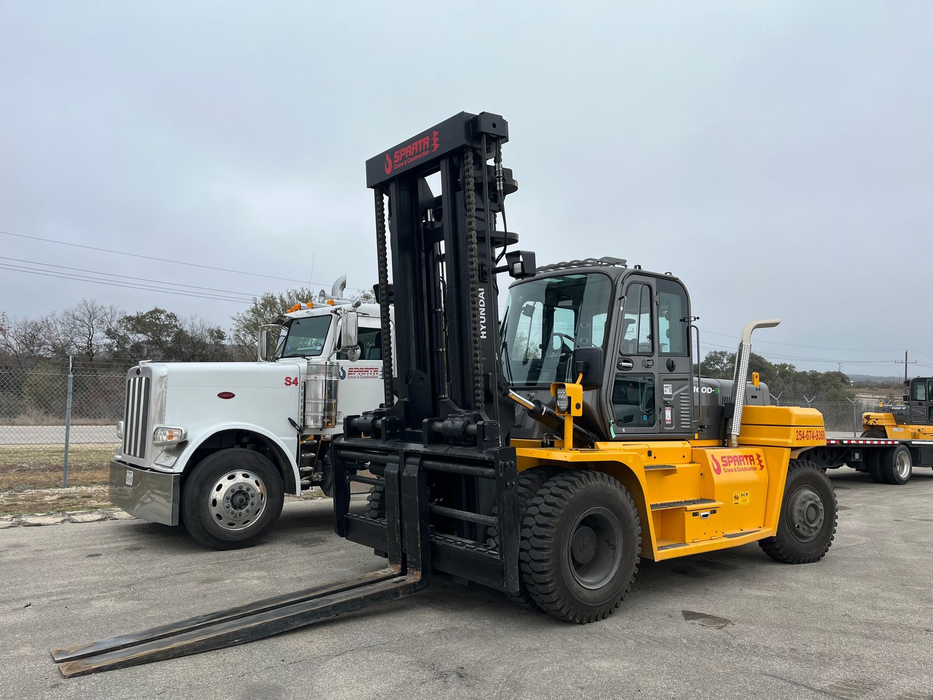 A yellow forklift is parked next to a white truck in a parking lot.