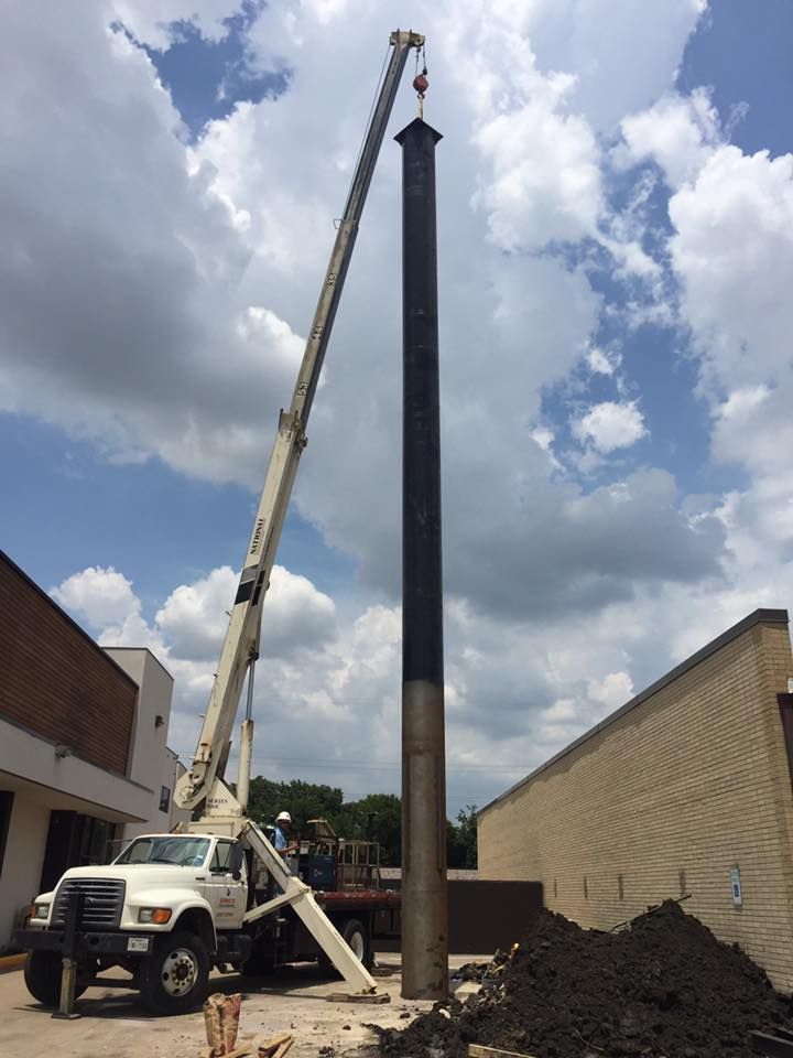 A crane is lifting a large pipe in front of a building.