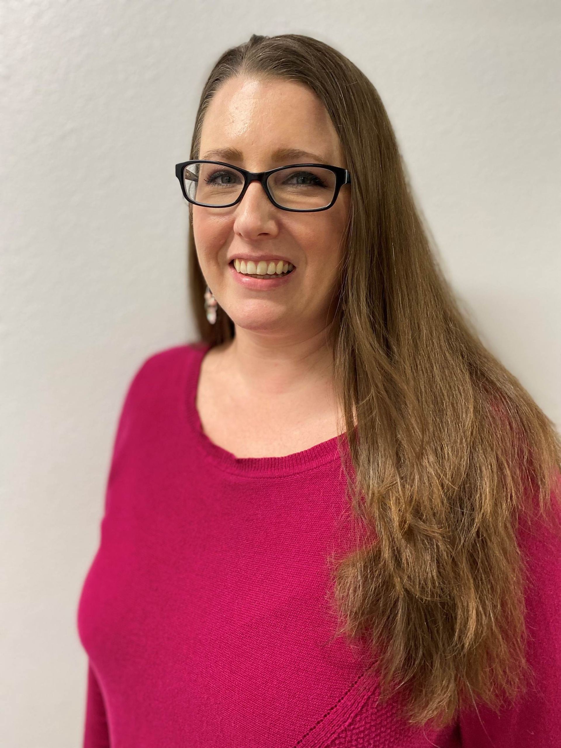 A woman wearing glasses and a pink sweater is smiling for the camera.