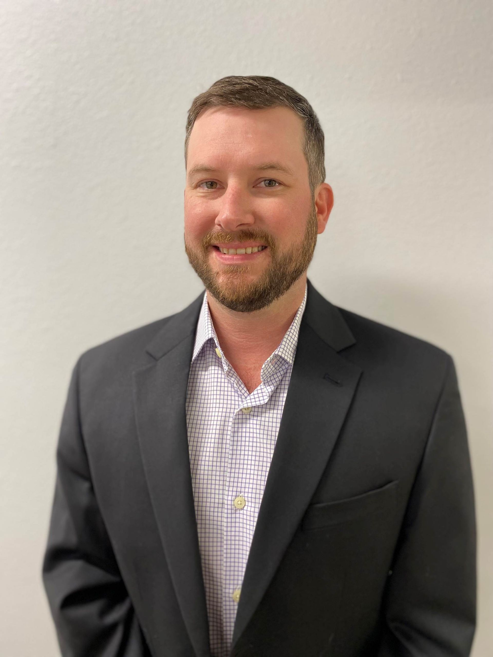 A man with a beard is wearing a suit and smiling for the camera.
