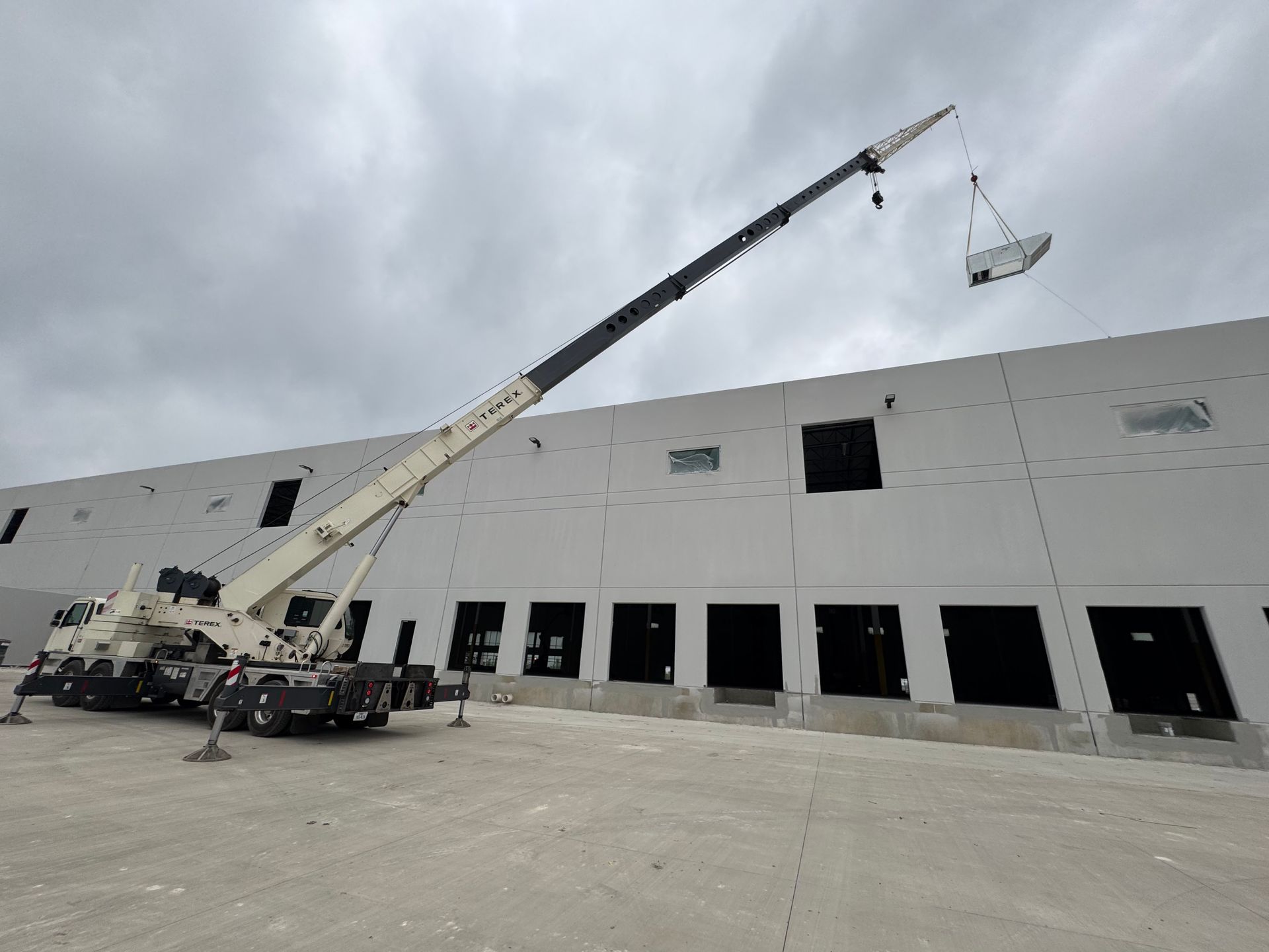 A large crane is lifting a large object in front of a large building.