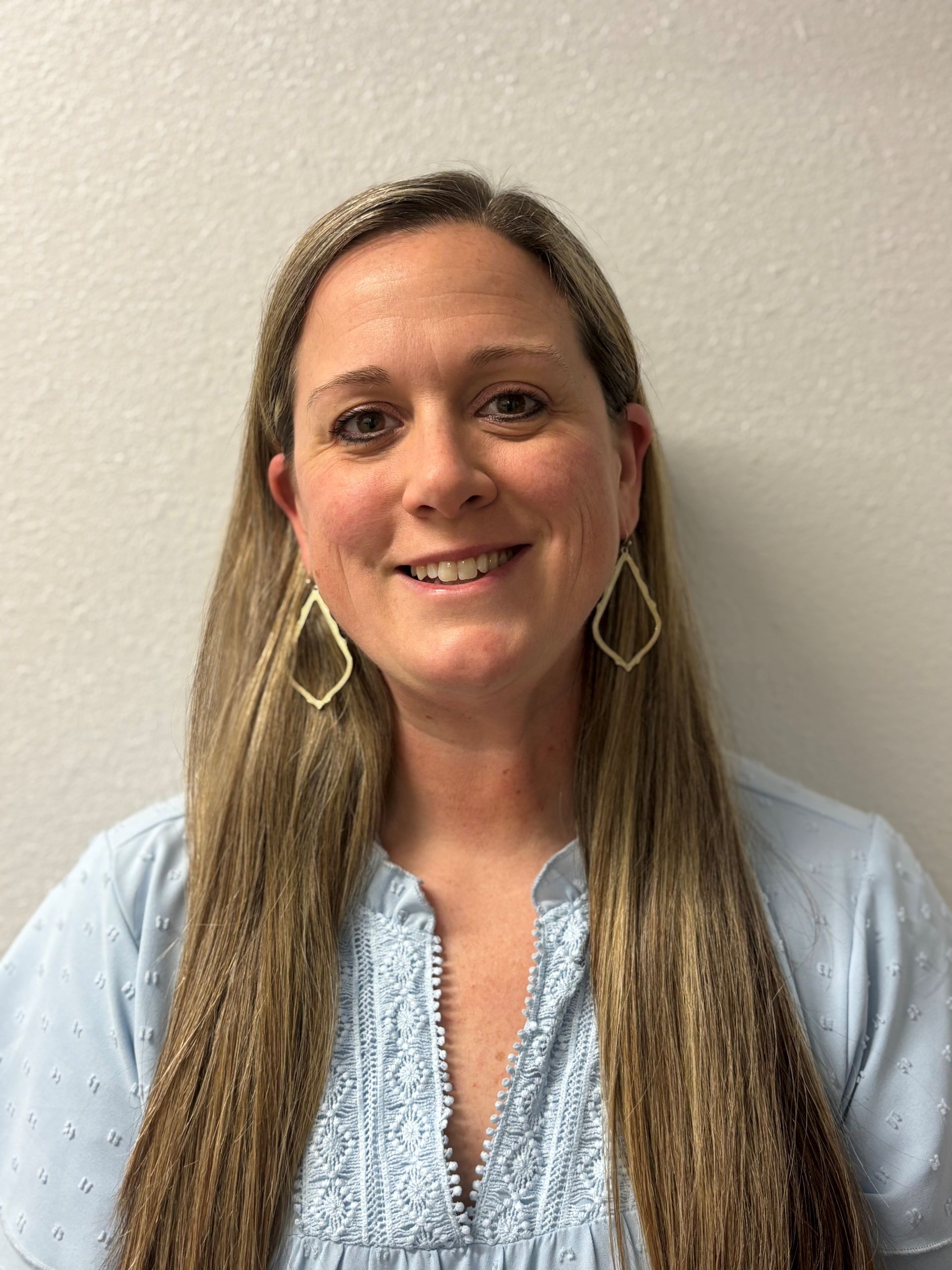 A woman with long hair and earrings is smiling for the camera.