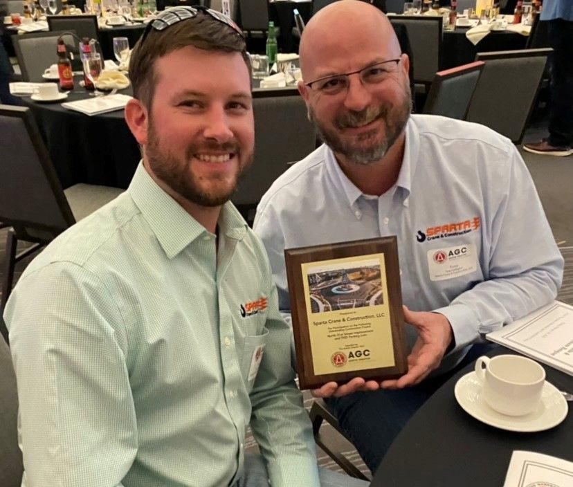 Two men are sitting at a table holding a plaque.