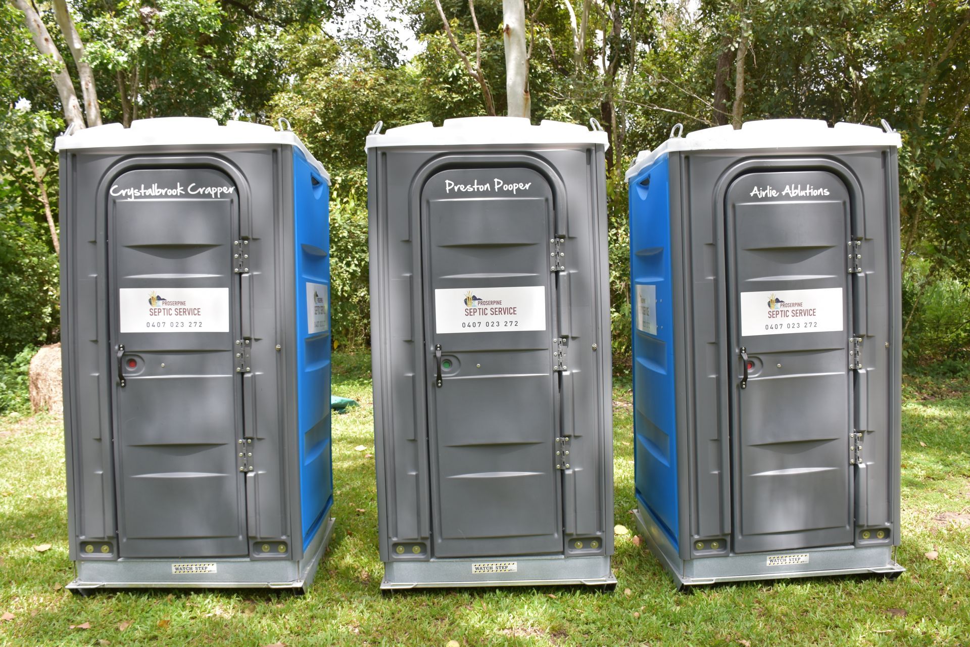 Three Portable Toilets Are Lined Up in a Grassy Field — Proserpine Septic Service In Airlie Beach, QLD