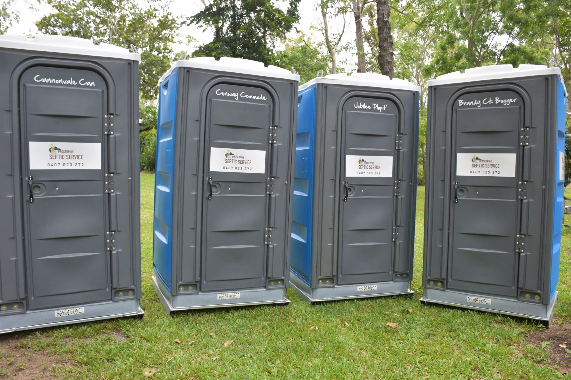 Three Portable Toilets Are Lined Up in a Grassy Field — Proserpine Septic Service In Cannonvale, QLD