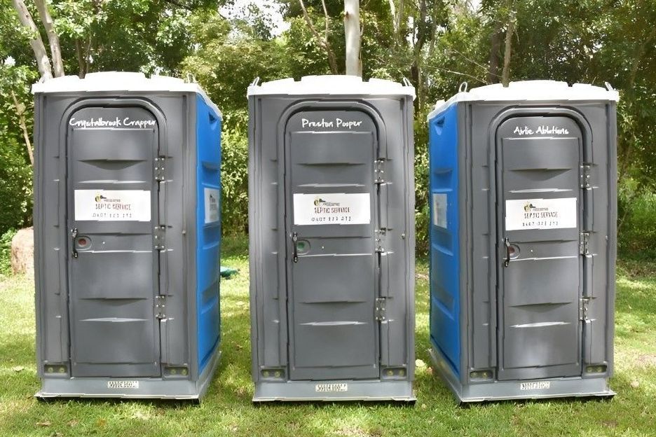 Three Portable Toilets Are Lined Up in a Grassy Field — Proserpine Septic Service In Proserpine, QLD