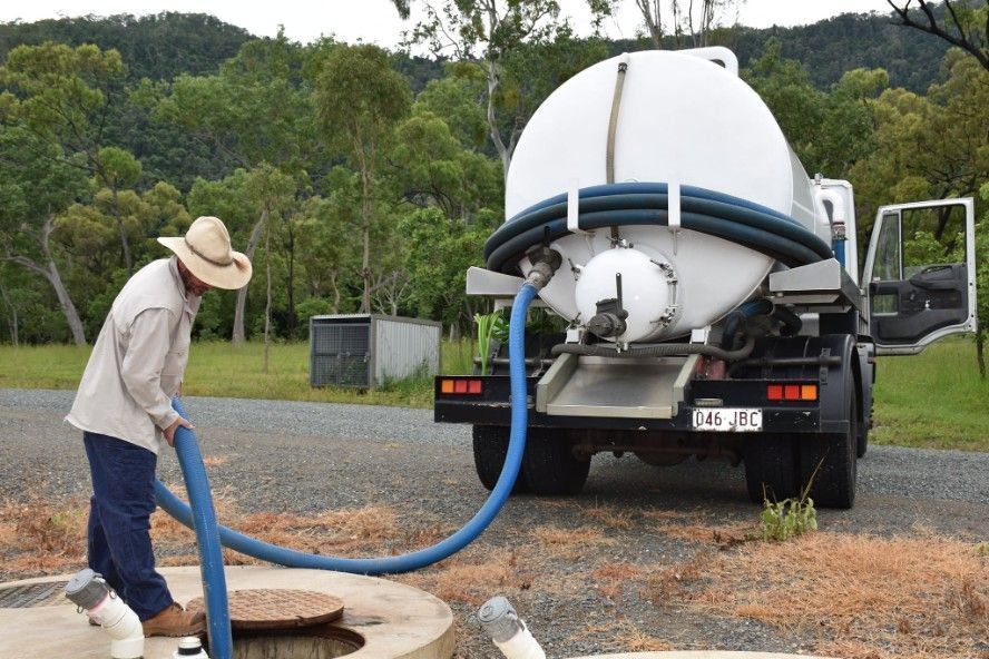 A Man in a Hat is Pumping Water — Proserpine Septic Service In Airlie Beach, QLD