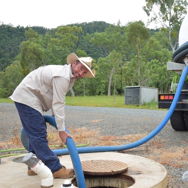 A Man in a Cowboy Hat is Clearing Septic Into a Manhole Cover — Proserpine Septic Service In Airlie Beach, QLD