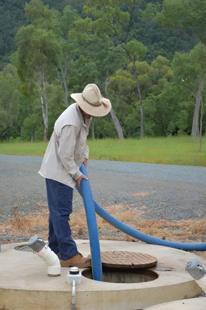 A Man in a Cowboy Hat is Pumping Water Into a Manhole Cover — Proserpine Septic Service In Cannonvale, QLD