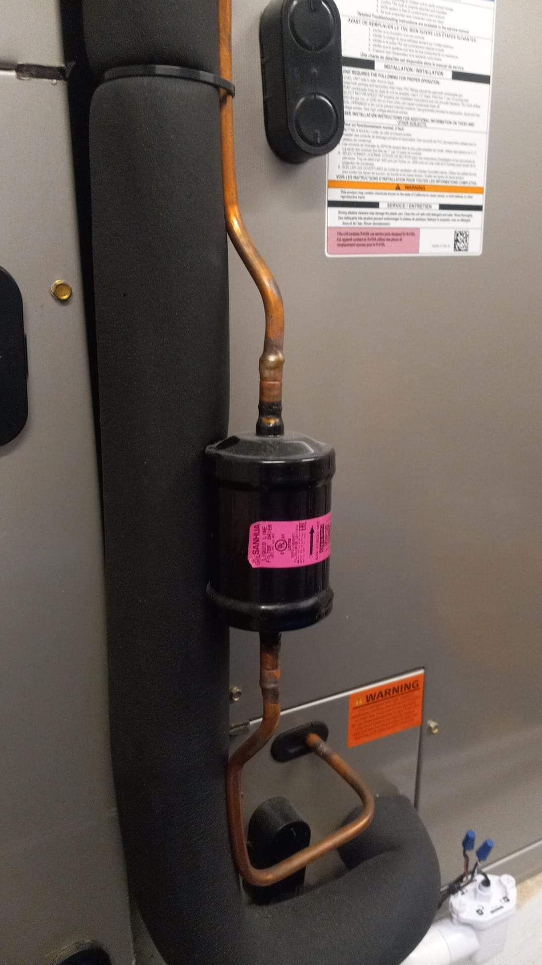 Man in white shirt and camo hat working on Carrier AC unit outdoors.