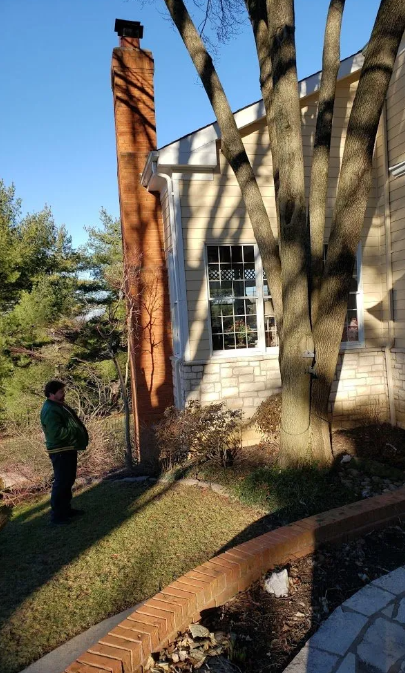 A man is standing in front of a house with two chimneys.