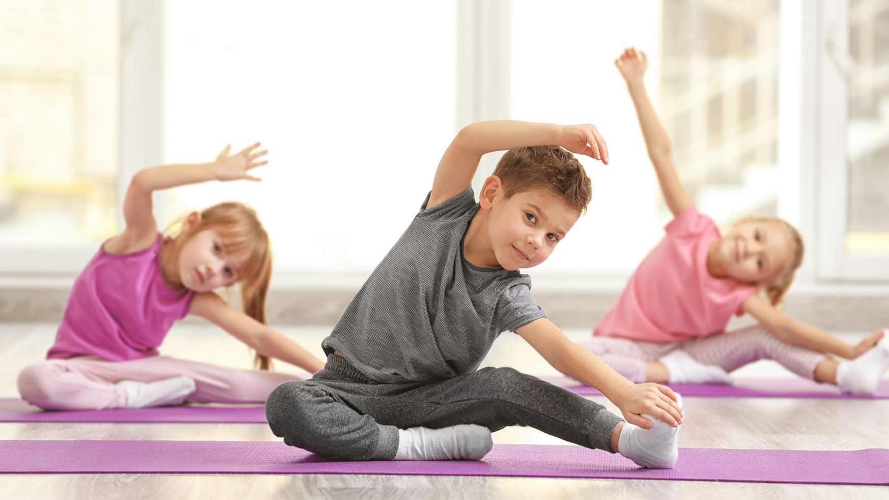 A group of children are sitting on yoga mats in a gym.