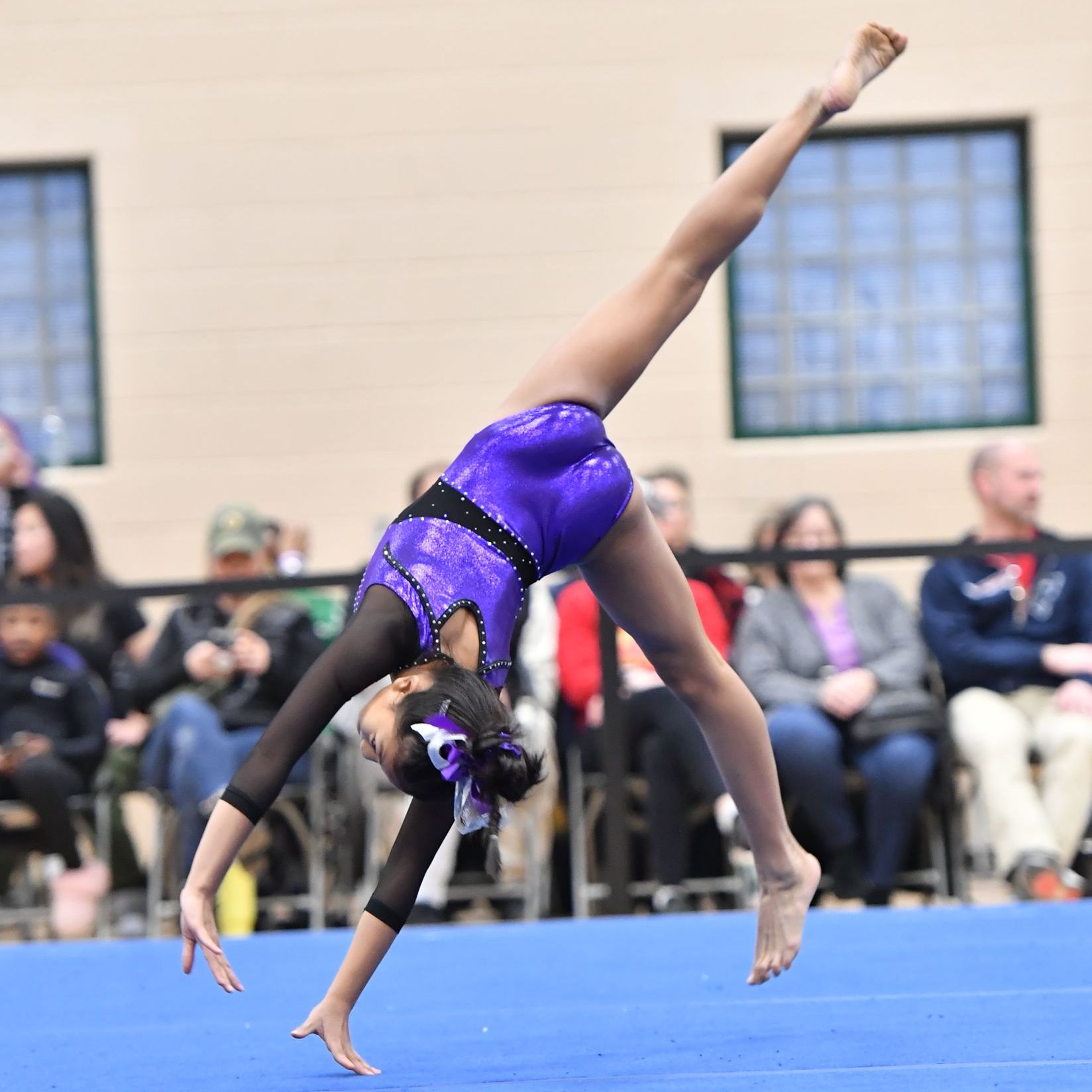 A gymnast in a purple leotard is doing a handstand on a blue mat