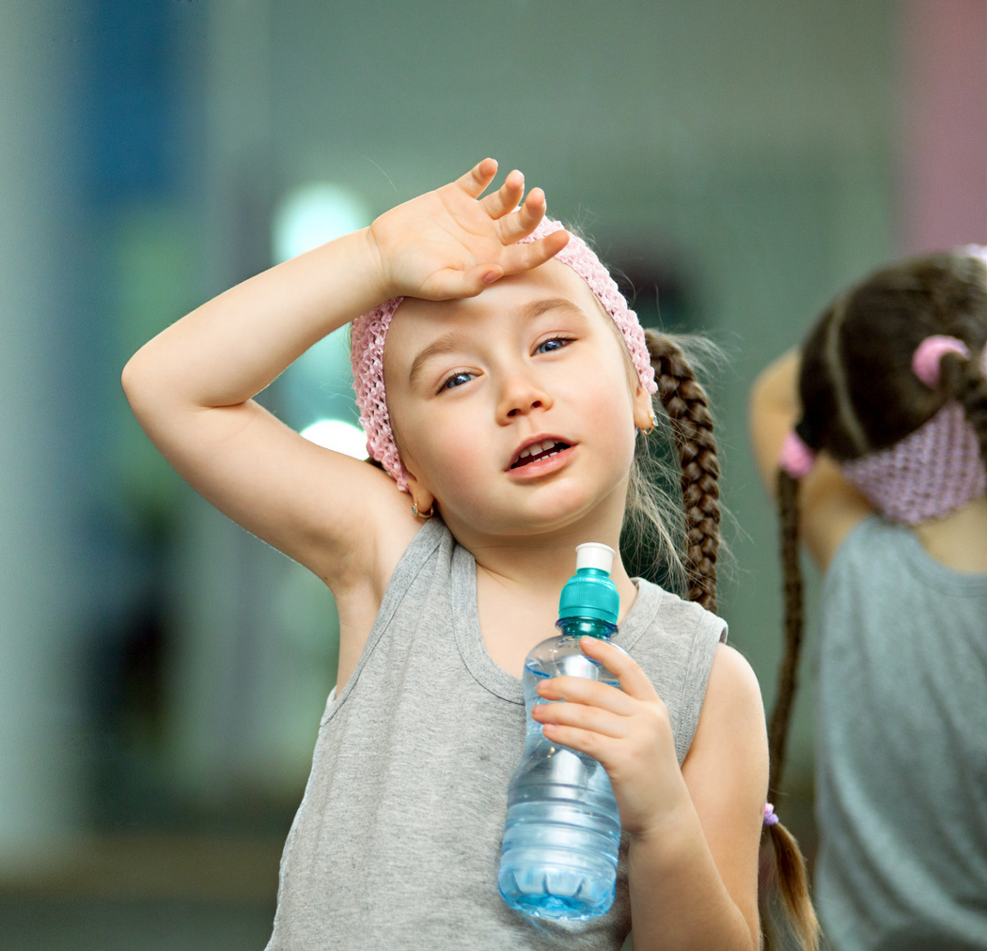 A little girl wipes her forehead with her hand while holding a bottle of water