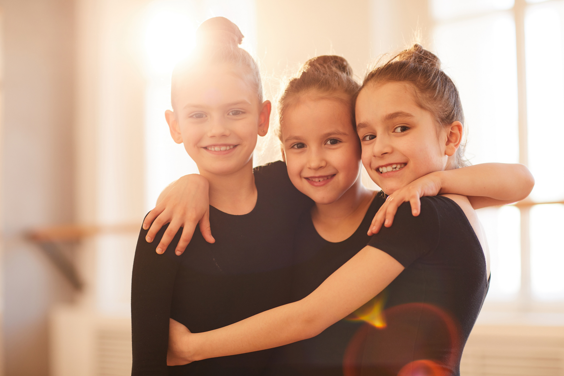 Three little girls are hugging each other in a dance studio.