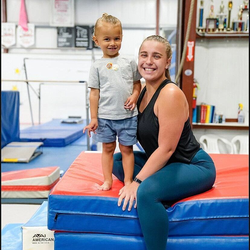 A woman and a child are sitting on a mat in a gym.