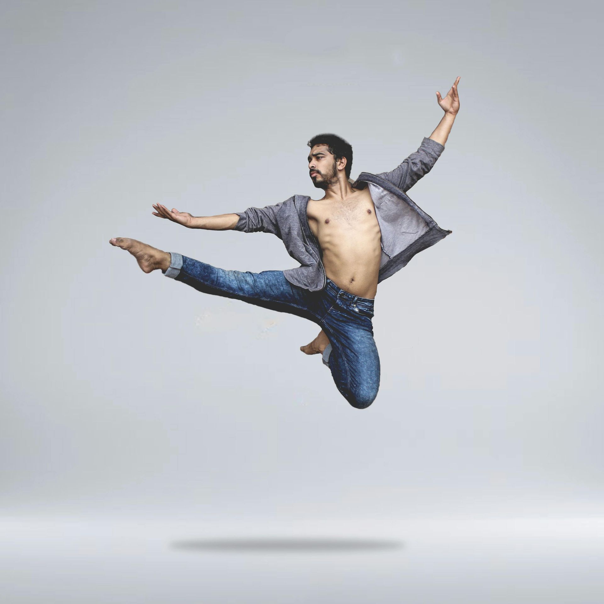 A shirtless man is jumping in the air with his arms outstretched