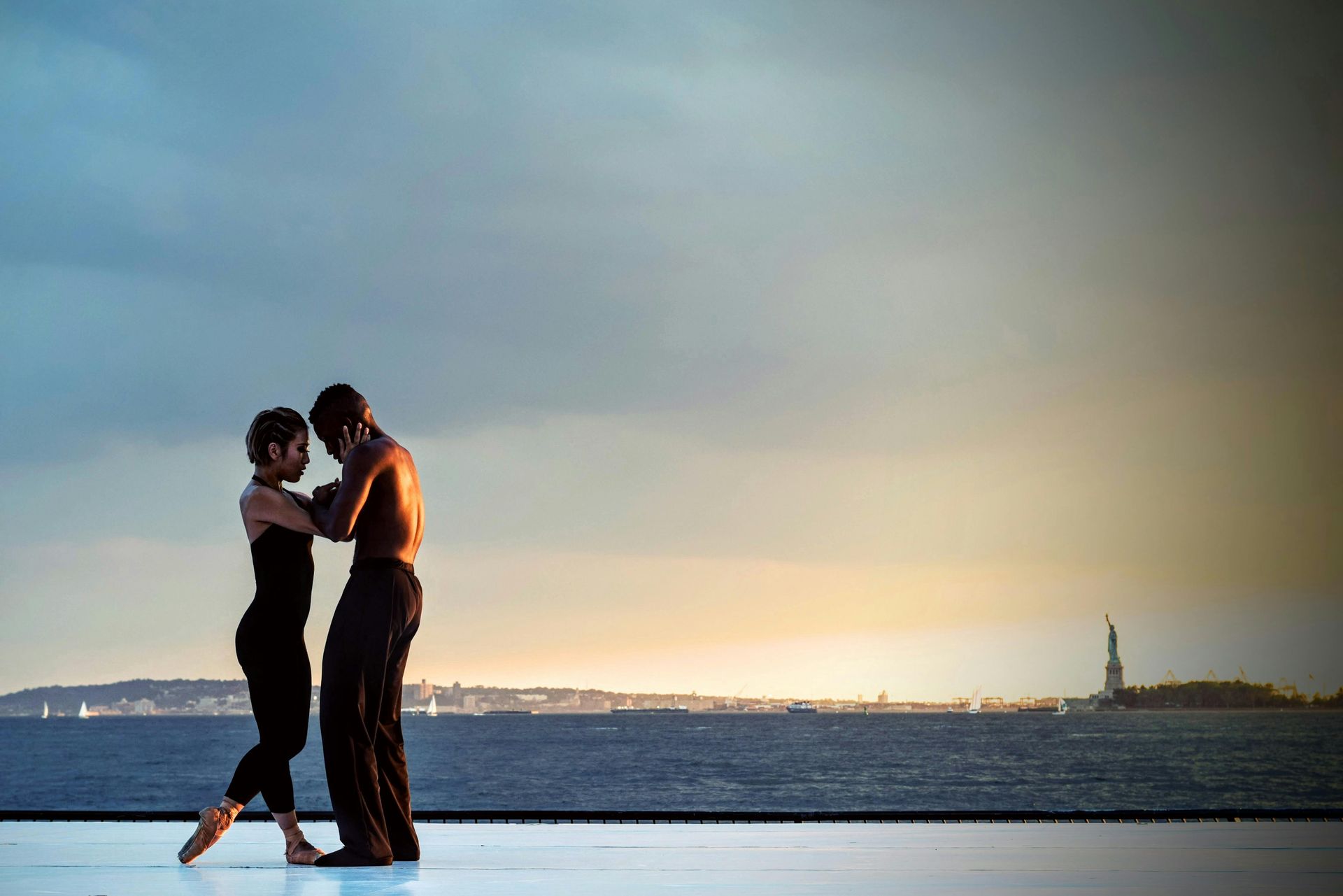 A man and a woman are dancing in front of a body of water.