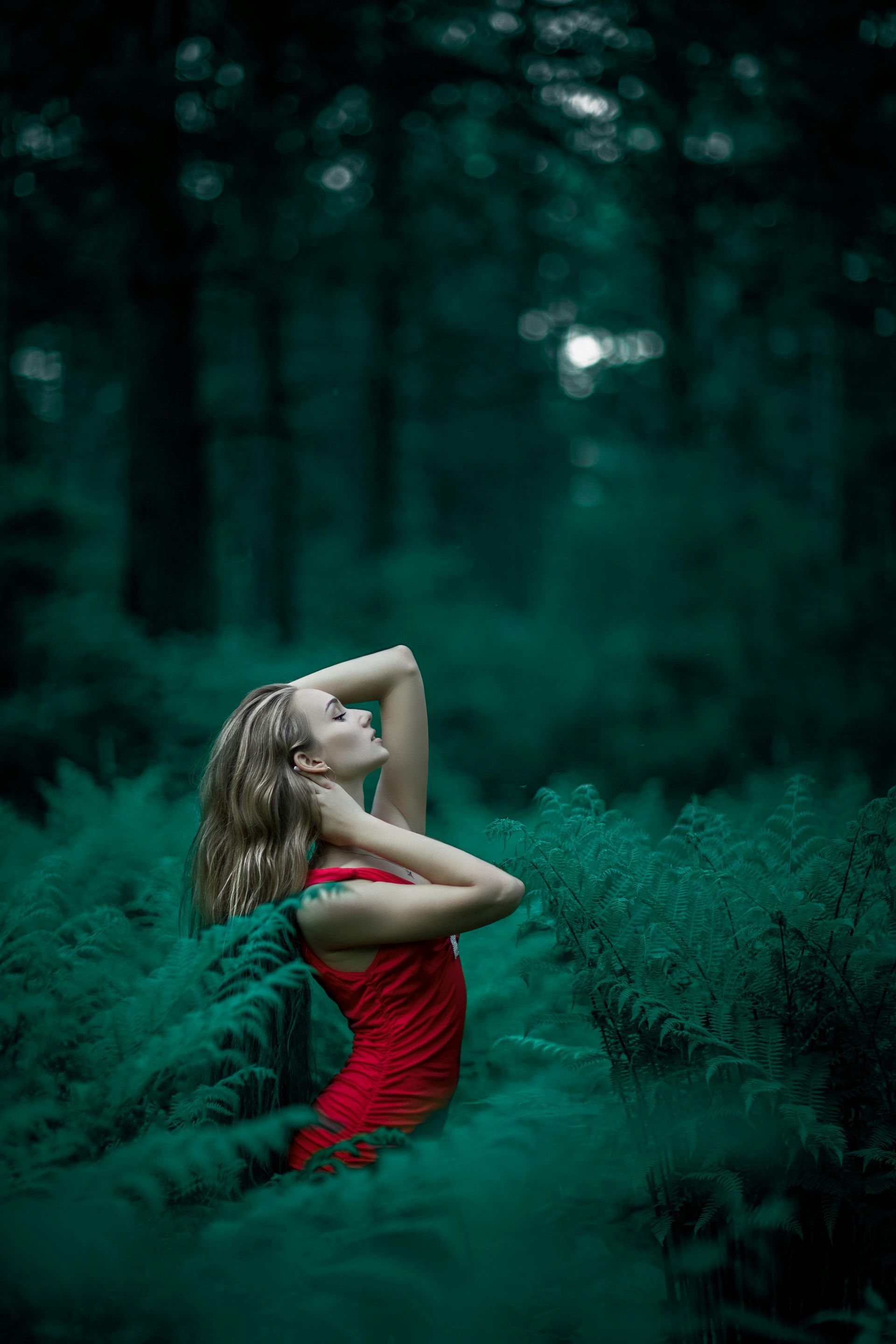 A woman in a red dress is kneeling in the woods.