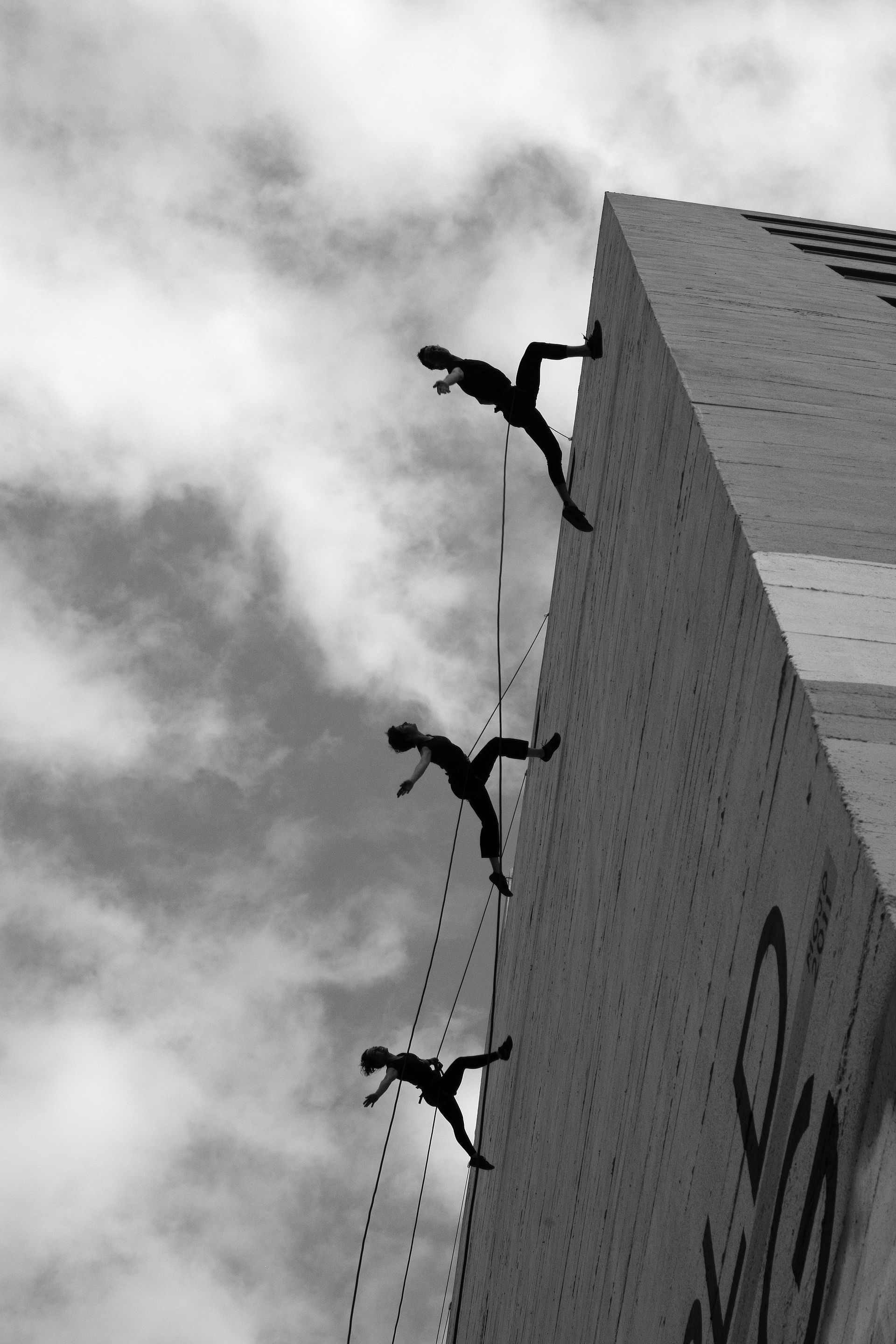 A black and white photo of people climbing up the side of a building
