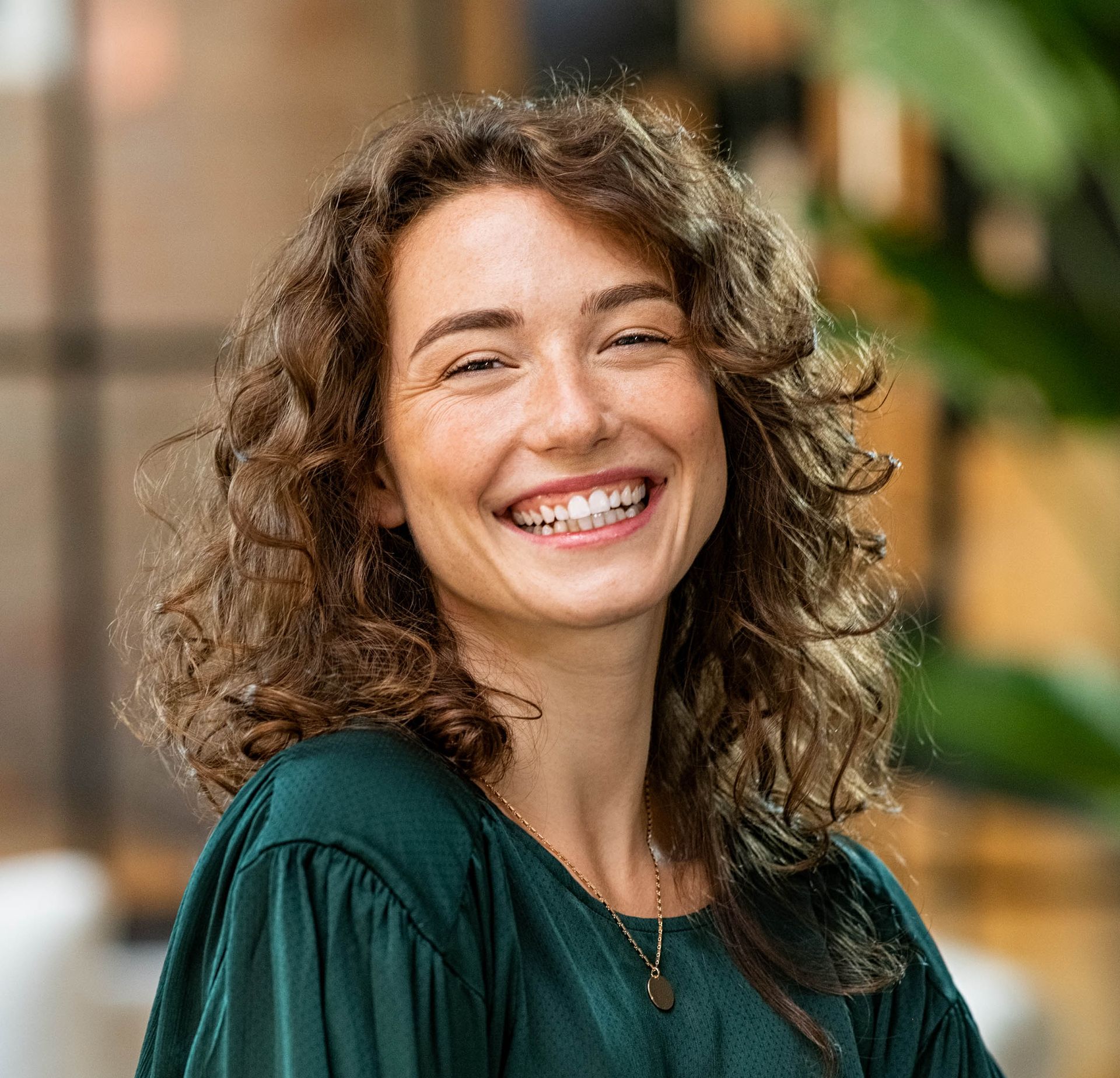 A woman with curly hair is smiling and wearing a green shirt.