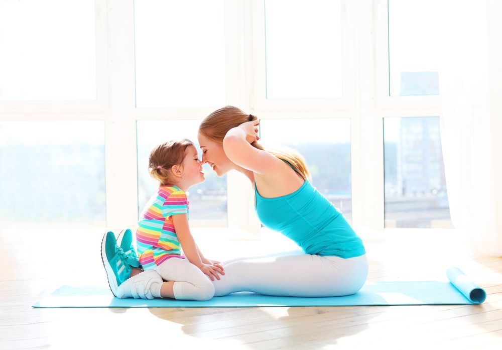 A woman and a little girl are sitting on a yoga mat.