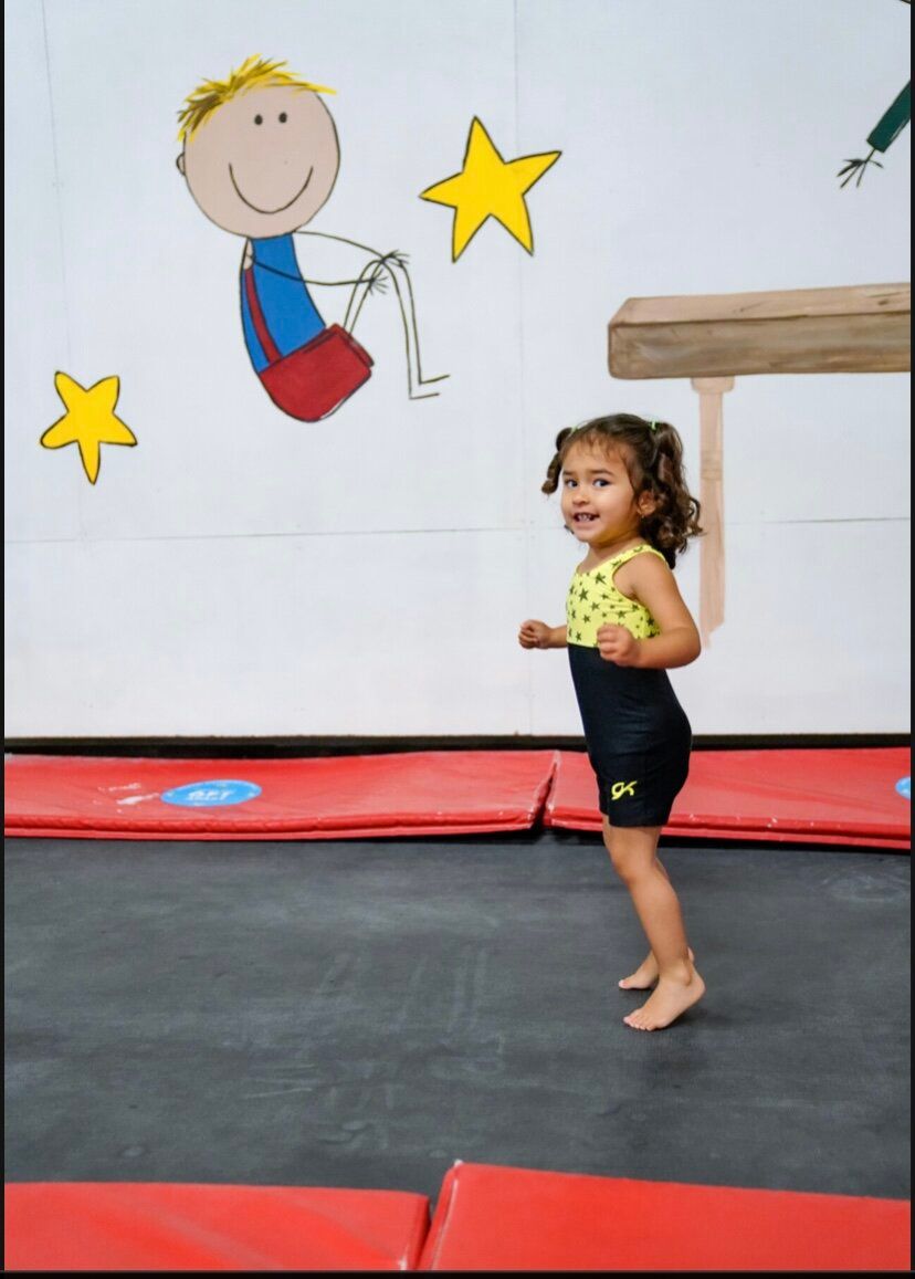A little girl is standing on a trampoline in front of a drawing of a boy on a balance beam