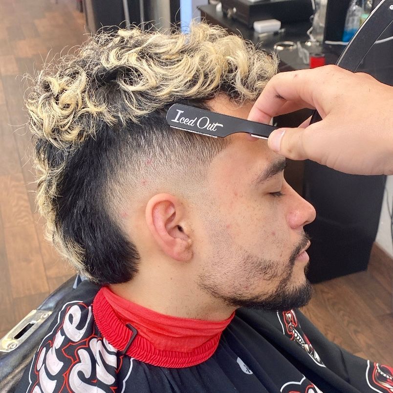 Man getting his hairline shaped with a razor by a barber. Hair is black and blonde. Close-up profile.