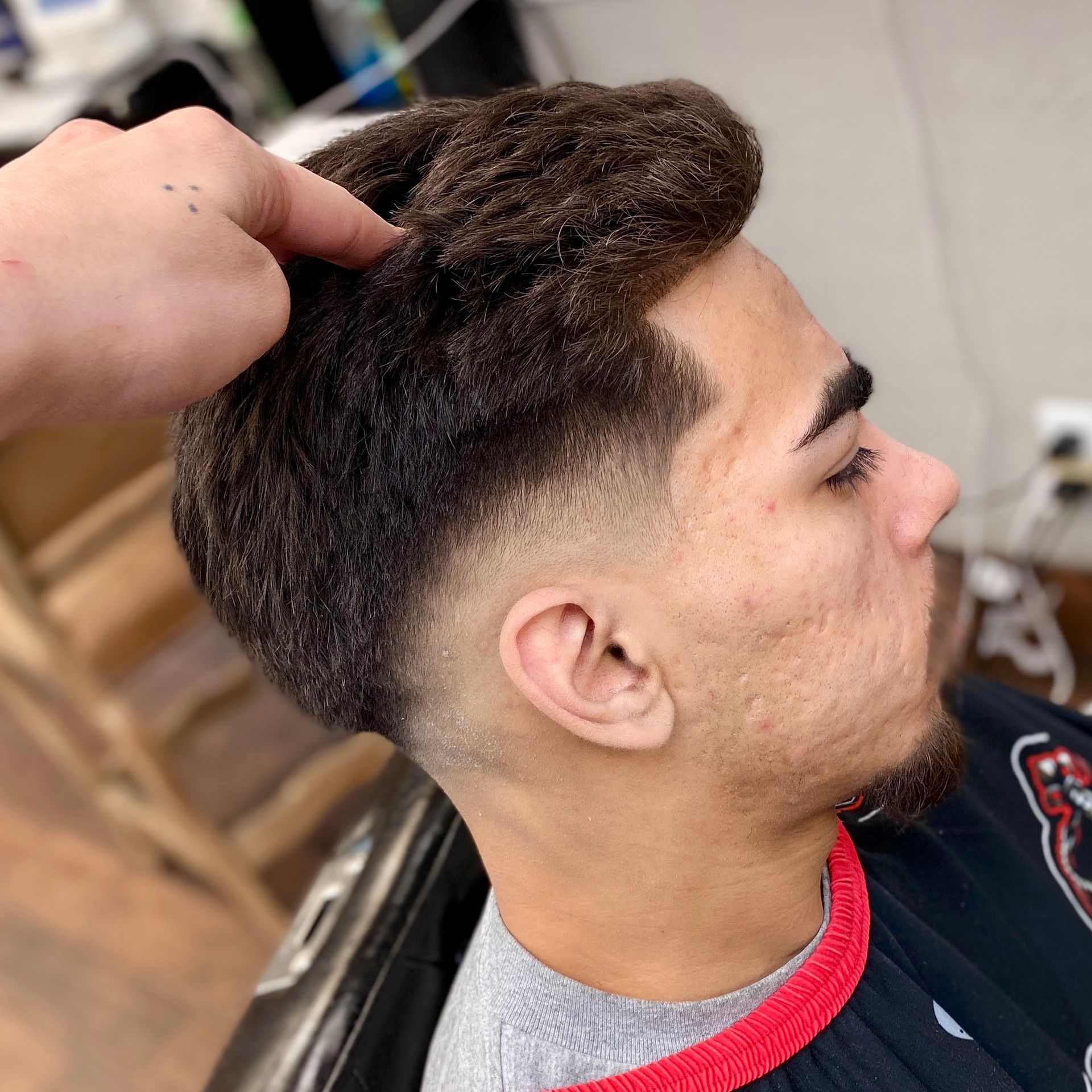Man with a faded haircut, hair styled up. A hand is touching his hair in a barber shop setting.