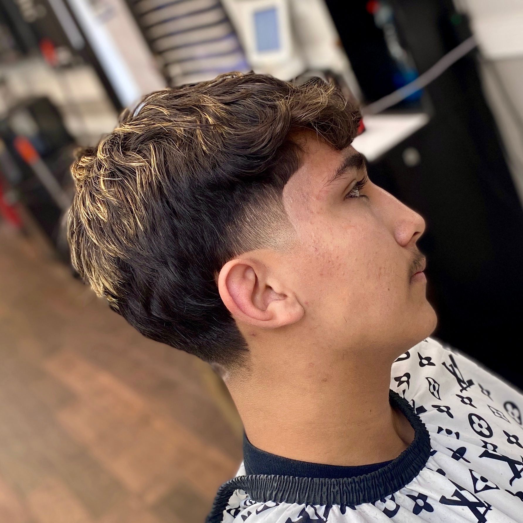 Person with a dark wavy hairstyle and faded sides, wearing a black and white patterned cape.