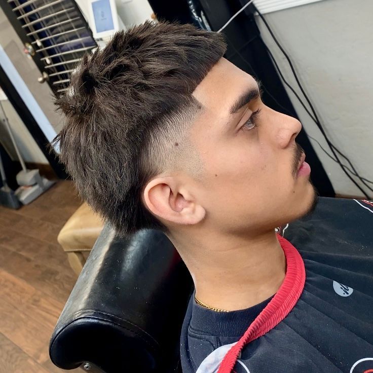Man with a textured haircut, low fade, and short mustache sitting in a barber chair.